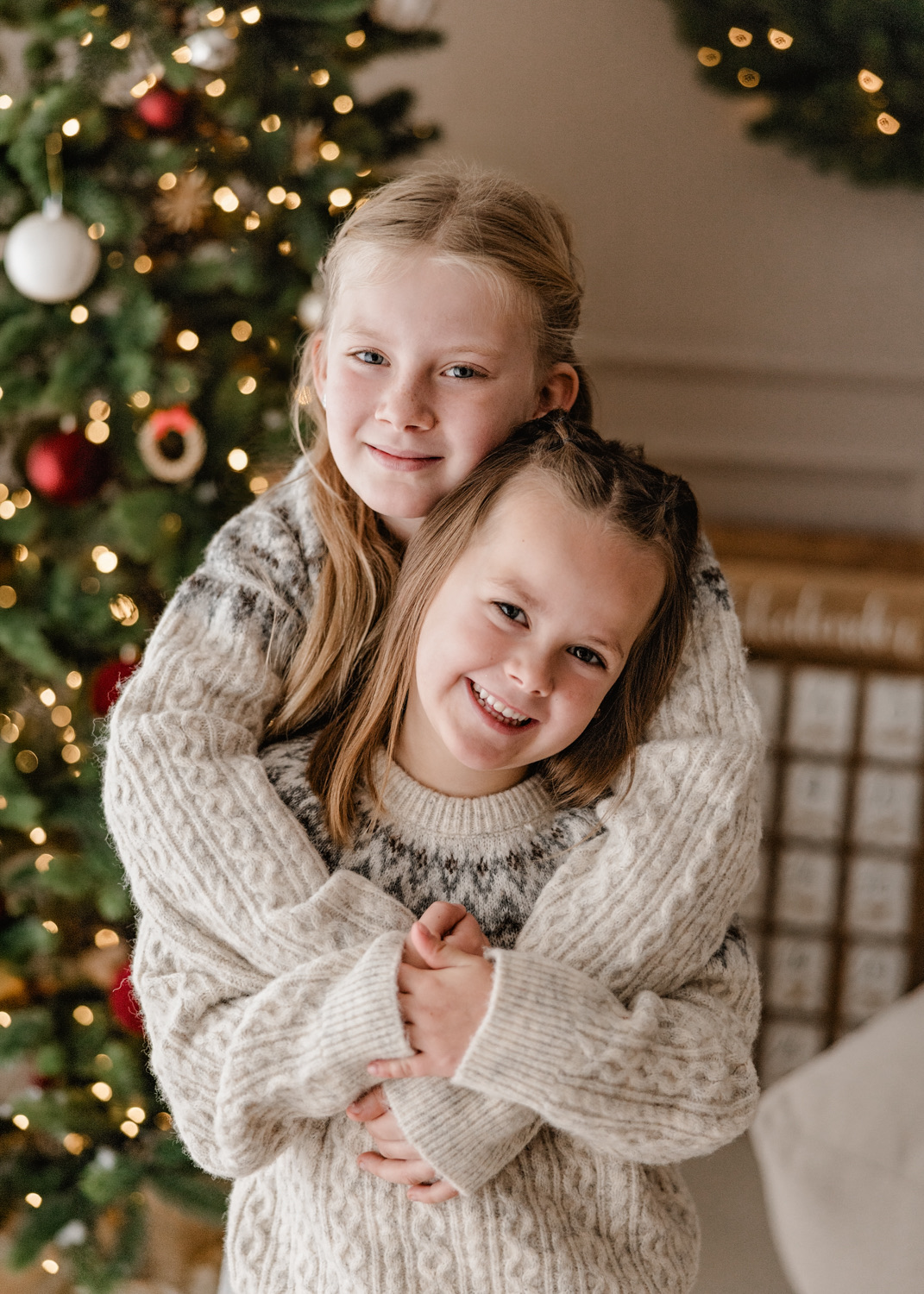 Zwei Schwestern kuscheln vor dem Weihnachtsbaum